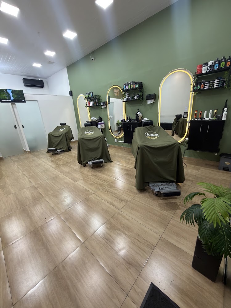 Salão da Brother's Barbearia com três cadeiras cobertas por capas verdes, espelhos ovais iluminados e parede verde com produtos nas prateleiras