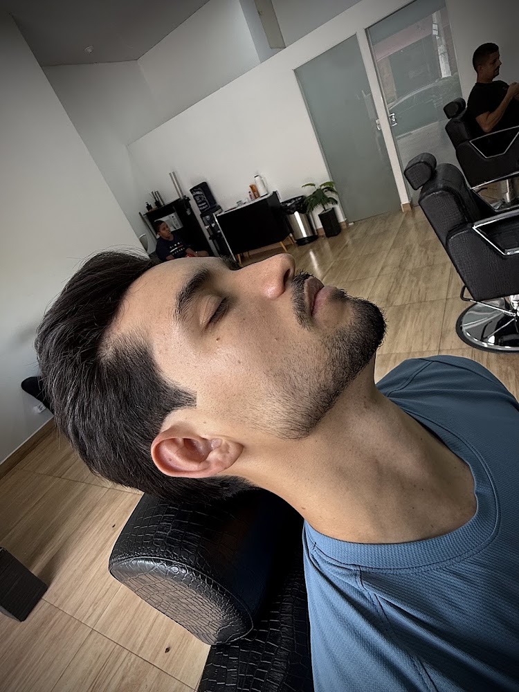 Cliente recostado na cadeira da Brother's Barbearia, com o salão e outra cadeira de barbeiro ao fundo